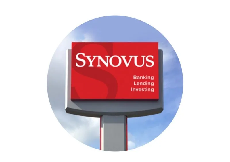 A red and white sign displays the text "Synovus" along with the words "Banking Lending Investing" against a blue sky.